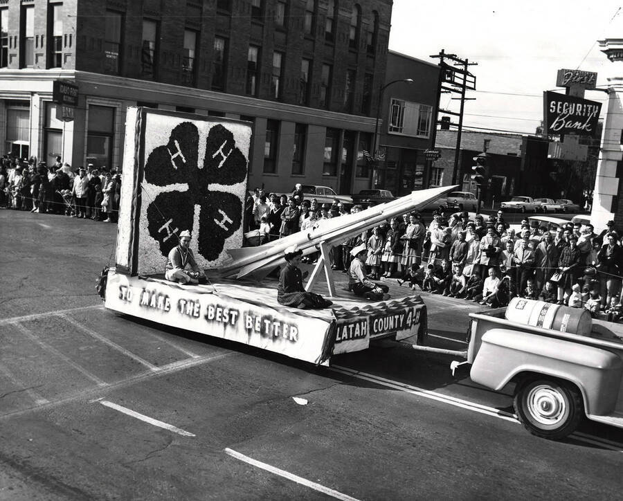 Four children sit on a 4-H float featuring a rocket during the Homecoming parade. The caption reads "To Make the Best Better." The photograph was taken in front of First Security Bank.