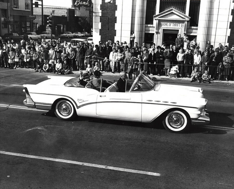 Grand Marshall Mr. and Mrs. Donald K. David ride in a car in the Homecoming parade in front of the First Security Bank.