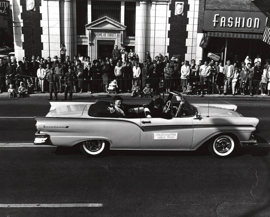 Congresswoman Gracie Pfrost rides in a car in the Homecoming parade in front of the First Security Bank and Fashion City.