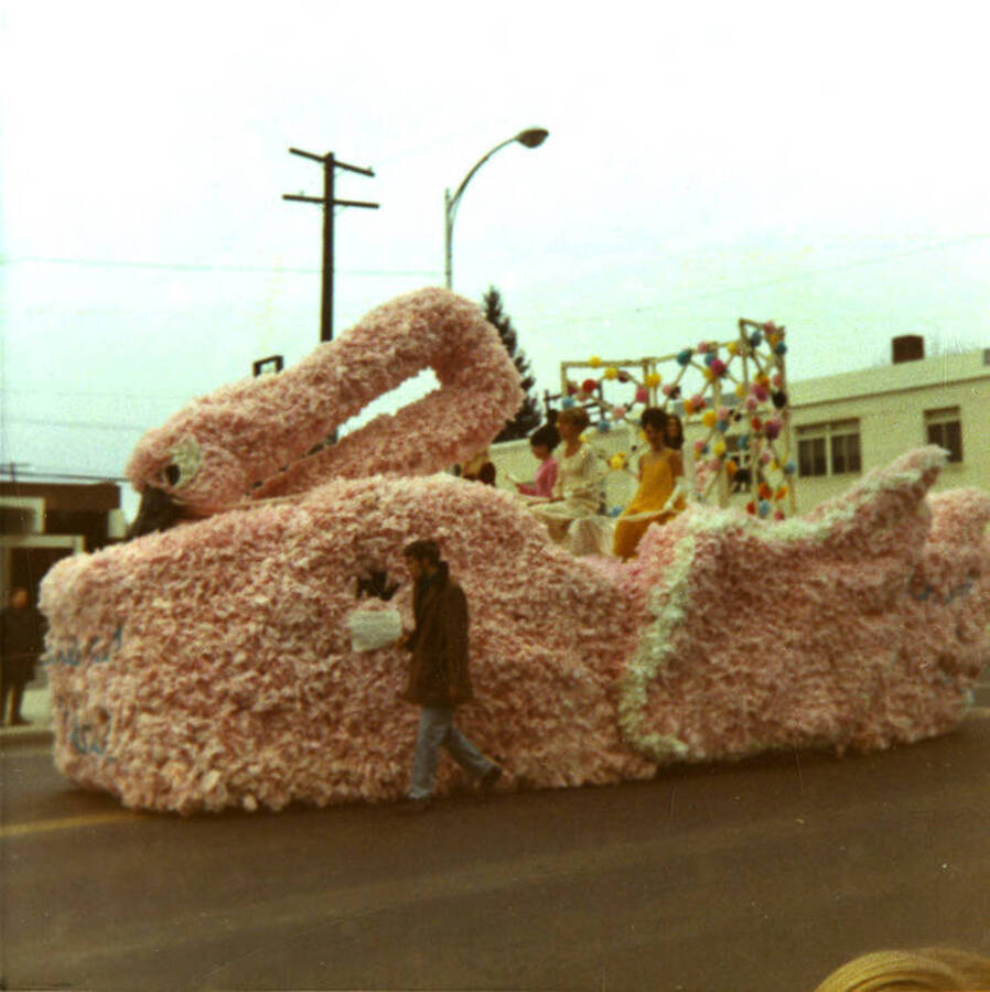 A group of women ride on a pink swan float while another person directs the car beneath during the Homecoming parade.