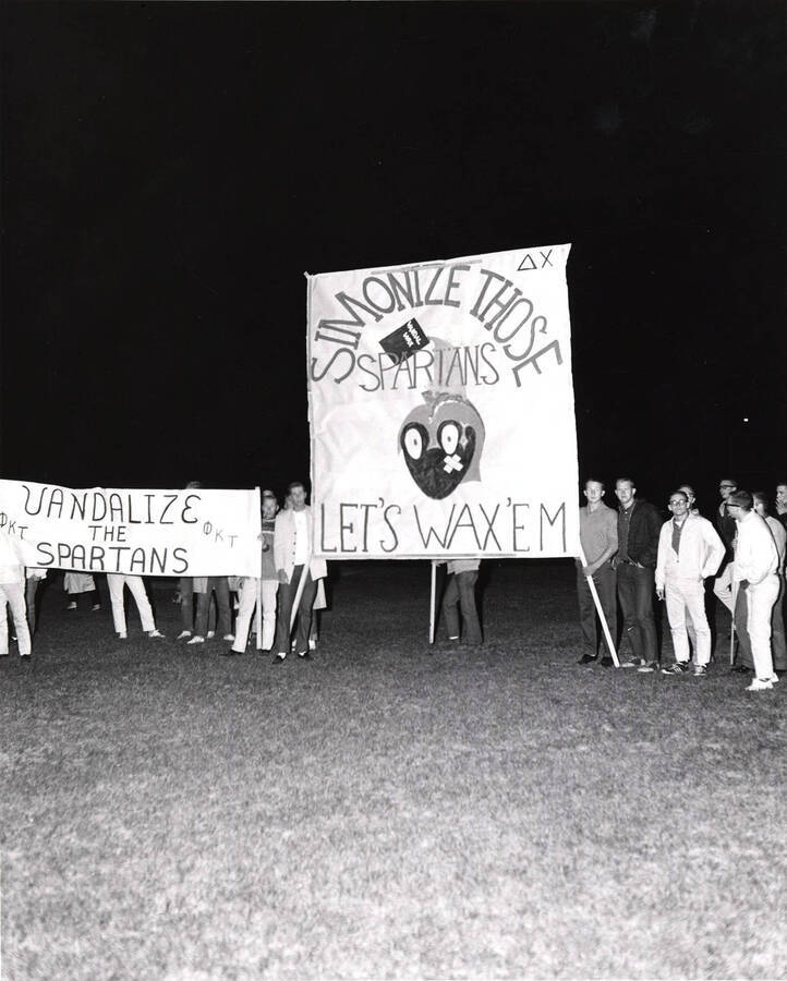 Students stand next to two signs that read "Vandalize the Spartans" "Simonize Those Spartans, Let's Wax 'Em" during the Homecoming bonfire.