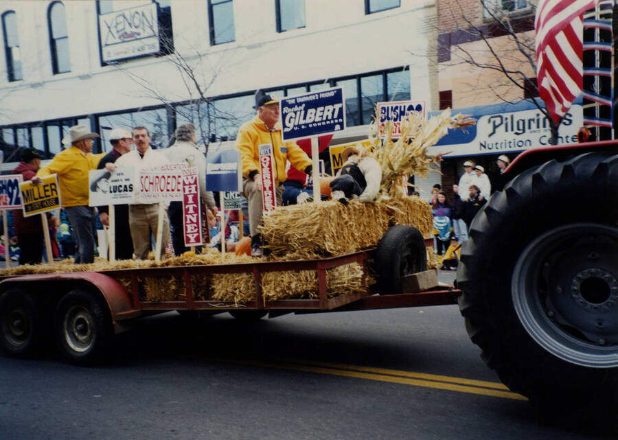 Men on hay bales hold signs for state and federal government position candidates as part of a float in the Homecoming parade.
