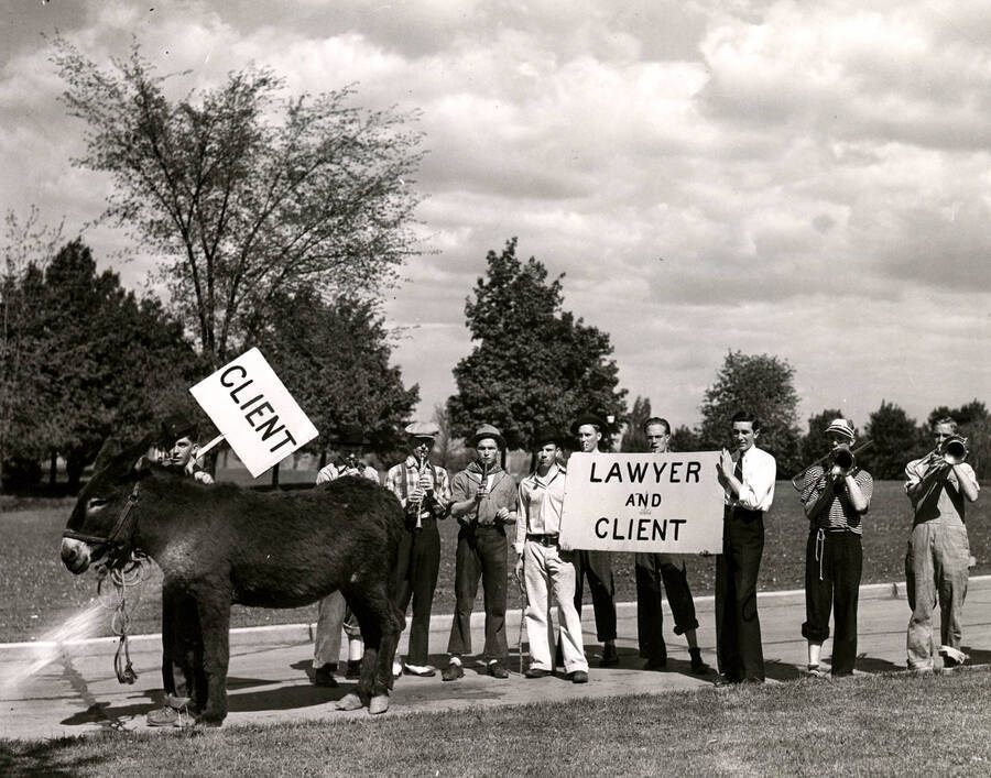 A student holds a sign reading 'client' next to a donkey while two other boys hold a sign reading 'lawyer and client' during Idaho's Little International Agriculture Show.