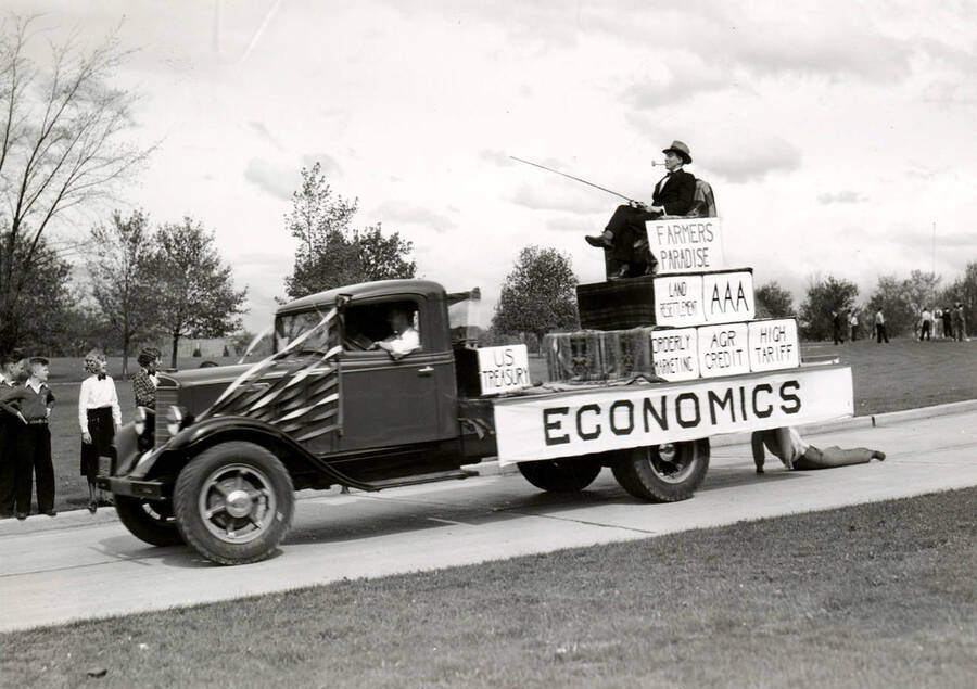 A man sits on a vehicle labeled ECONOMICS smoking a pipe and metaphorically fishing in the US Treasury box during Idaho's Little International Agriculture Show.