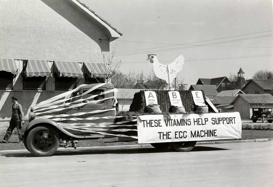 A truck sports an exhibit of a chicken with three bags of feed, each displaying a different essential vitamin. A sign reading 'These vitamins help support the egg machine' is posted on the side of this entry into Idaho's Little International Agriculture Show parade.