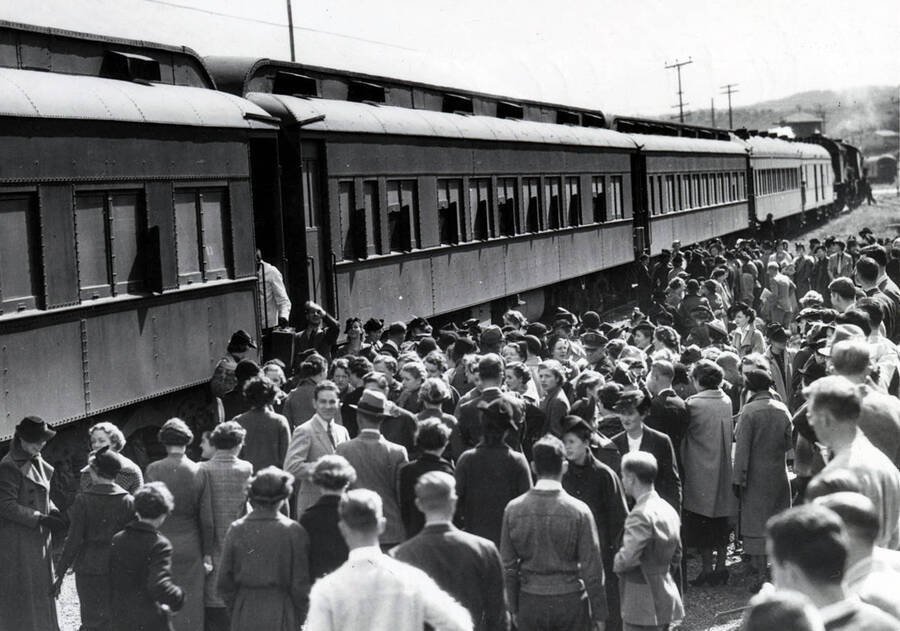 Large groups of people meet to disembark from and board the docked Student Special train.
