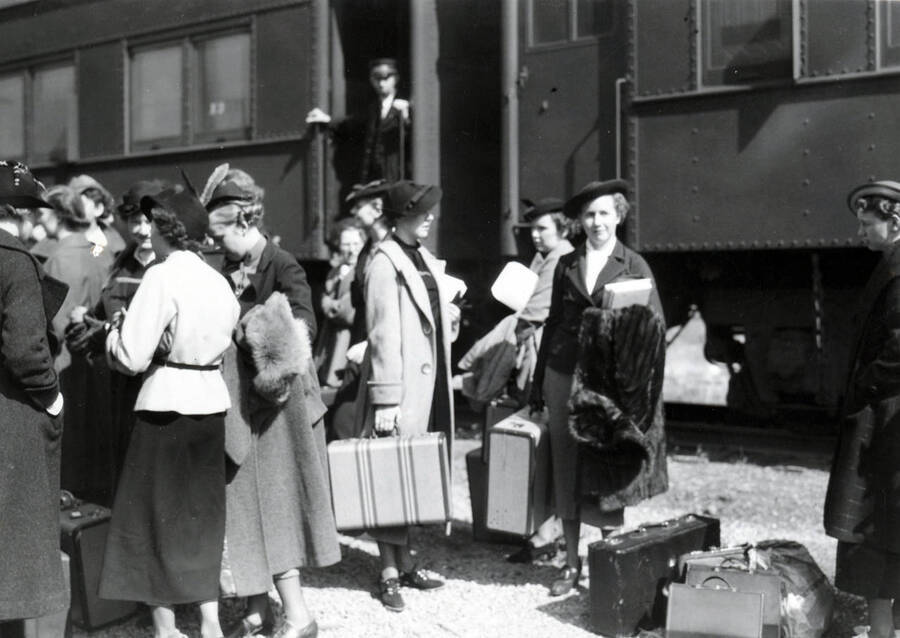 Several women holding luggage wait beside the Student Special train.