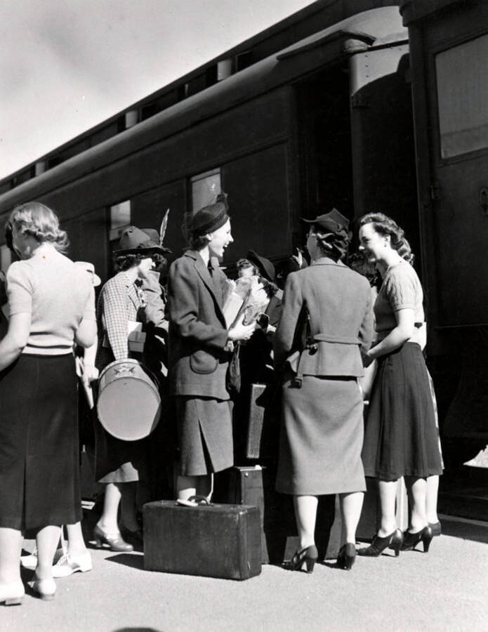 A group of women stand outside of the Student Special train, talking and laughing with their luggage on the ground.