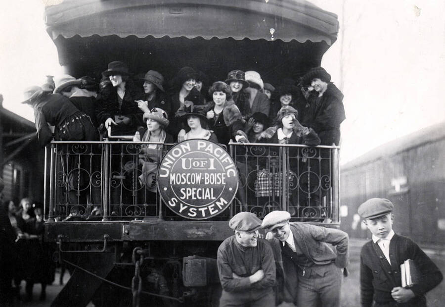 A group of students pose on and in front of the back of the Student Special train. A sign on the train reads 'Union Pacific System: U of I Moscow-Boise Special.'