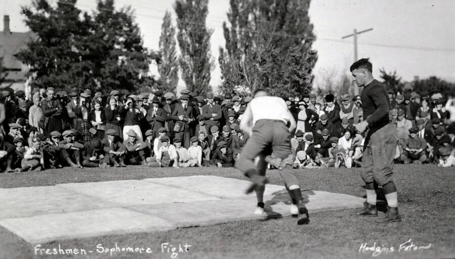 A referee looks on as two students fight on a mat during the Hulme fights. The caption on the photograph reads, 'Freshmen-Sophomore Fight.'
