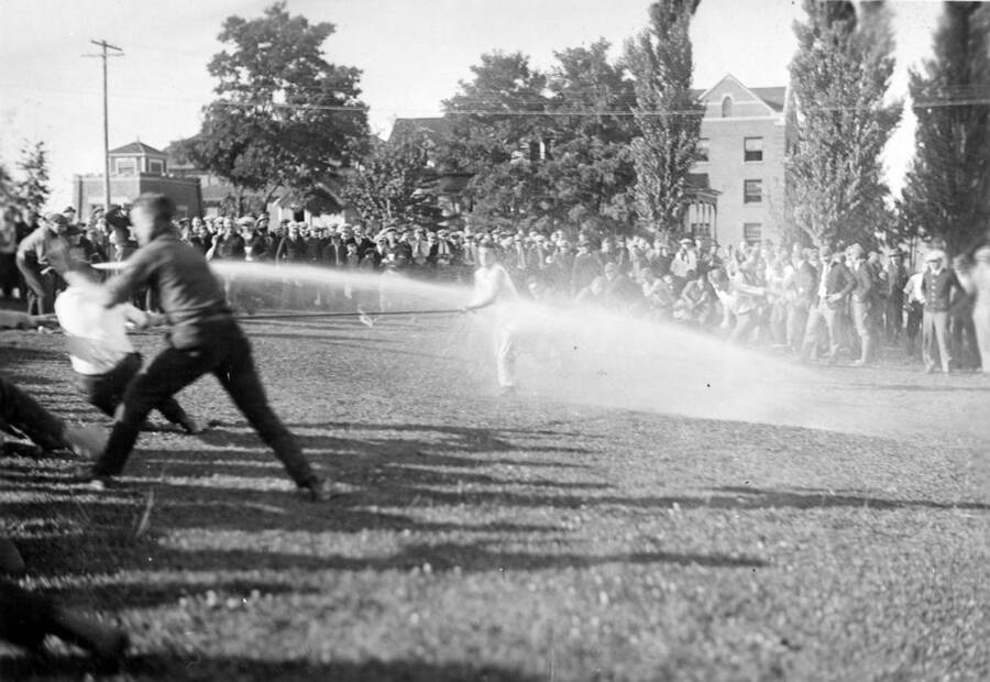 A crowd watches as freshman and sophomores compete in a tug-of-war contest during the Hulme contests. One student is seen being sprayed by a hose.