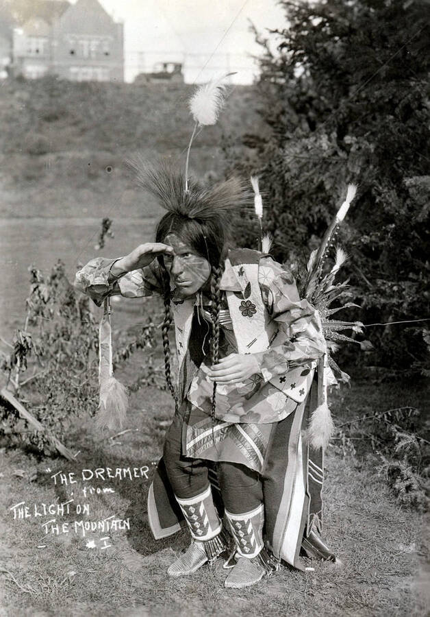 J. Ray Burbidge dressed in Native American garments peers toward the distance as part of the Light on the Mountains pageant. Caption reads: "'The Dreamer' from The Light on the Mountain #1."