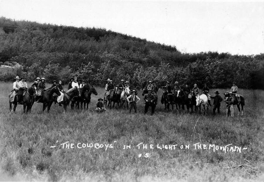 Several people, some on horses, pose in 19th century western wear for the Light on the Mountains pageant. Caption reads: "'The Cowboys' in The Light on the Mountain - #5."