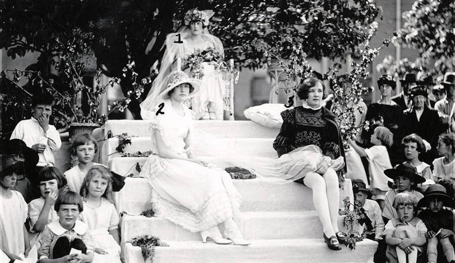 The May Queen sits with her court during Campus Day. Students pictured: 1) Agnes Cox (May Queen), 2) Mary Burleigh (Maid of Honor), 3) Mirth MacArthur (Page). The May Queen sits atop some steps with her court during Idaho's Campus Day.