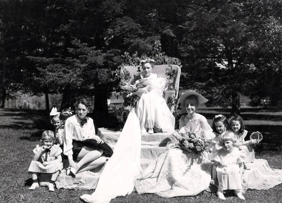Idaho May Queen Margaret Brodrecht sits atop a throne, surrounded by her court during Idaho's Campus Day celebrations. Students pictured: 1) Margaret Brodrecht (May Queen), 2) Jane Baker (Maid of Honor), 3) Donna-May South (page), 4) Ann DuSault (flower girl).