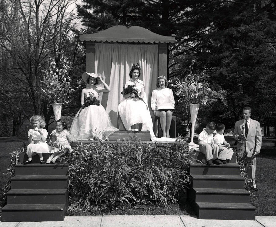 Queen Dolores Uria sits on a wooden throne, surrounded by her court, during Idaho's Mother's Day festivities. Students pictured: Betty Ruth Westerberg (Maid of Honor) to the Queen's left, Vonda Jackson (Page) to the Queen's right, Kalia Doner and Carol Dobler (Flower girls), Bill Parsons (A.S.U.I. president), Danny Kirkland and Stanley Hiserman (small boys).