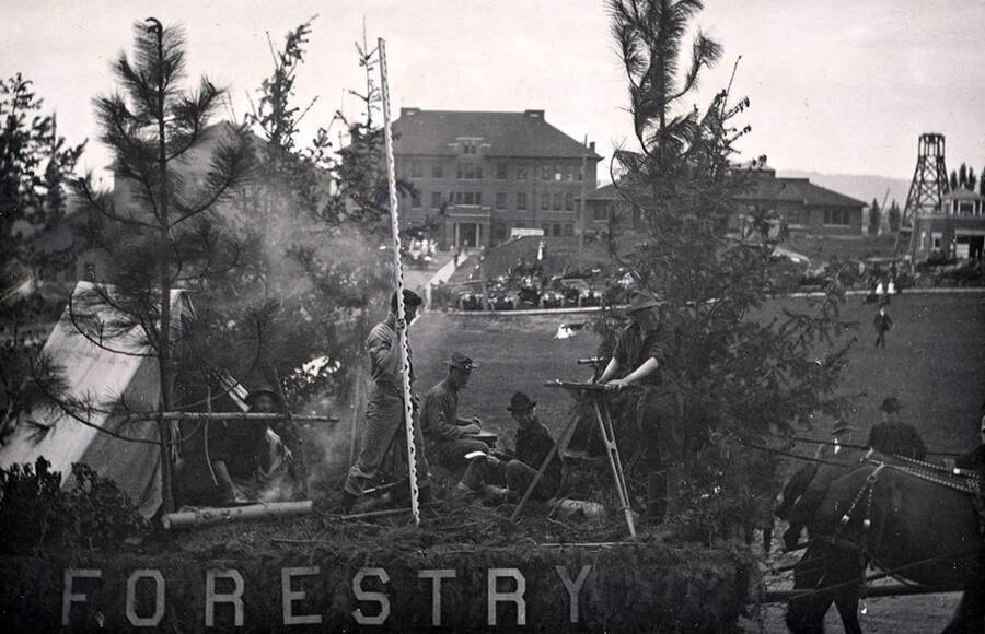 Students sit atop the forestry float, which is decorated with a tent and trees during Idaho's Campus Day parade. Morrill Hall can be seen in the background.