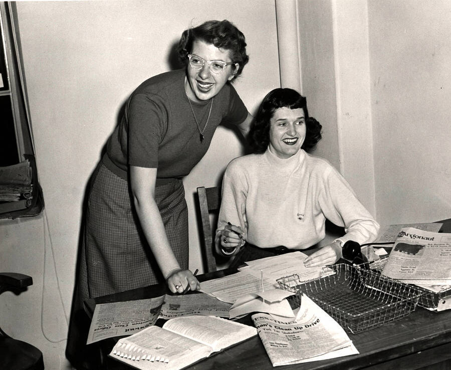 News editor Virginia Orazem and her successor, Sheila Janssen, work and laugh together at a desk scattered with issues of the Idaho Argonaut.