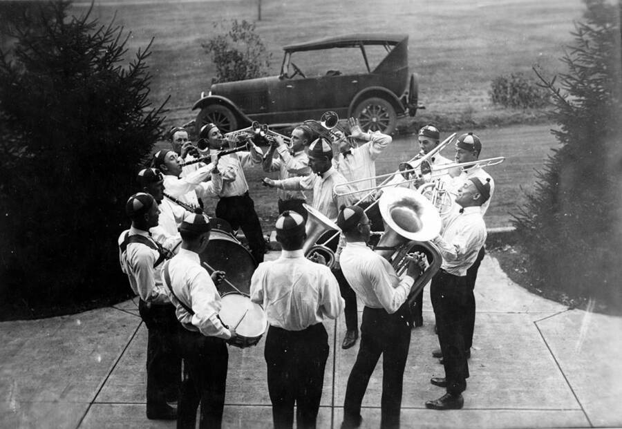 A man conducts a circle of pep band students. Francis C. Sheneberger pictured in the lower-right with a tuba.