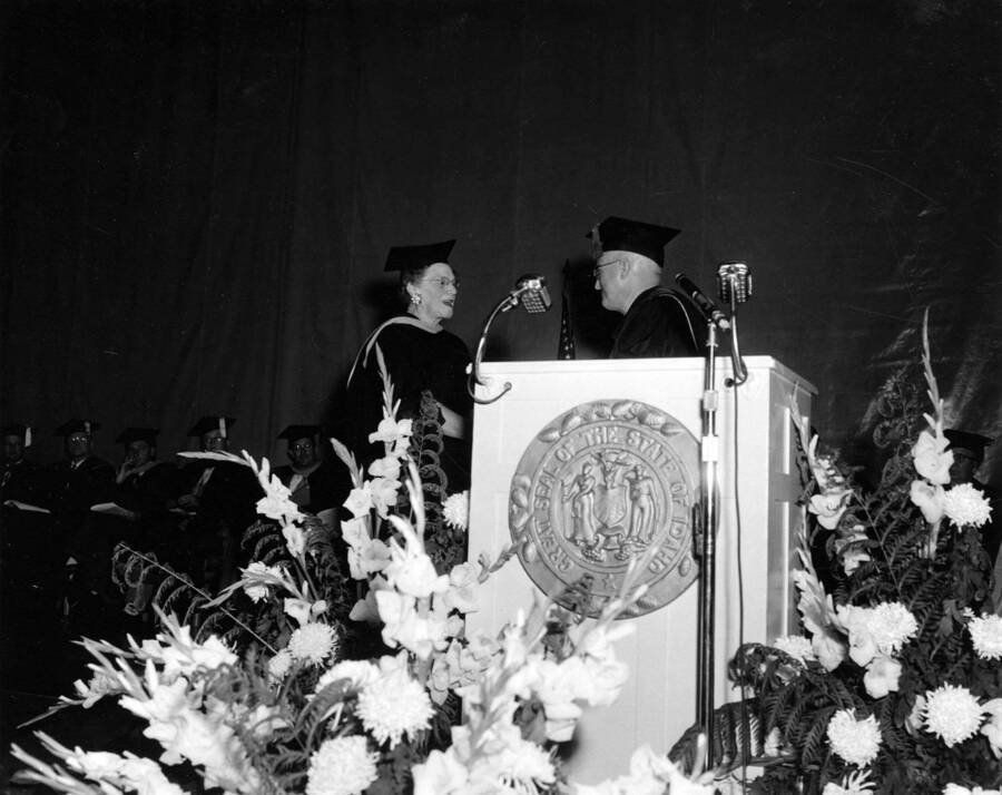 Amidst flowers, Idaho President Donald R. Theophilus shakes hands and awards Dean of Women Louise Carter the Citation of Merit.