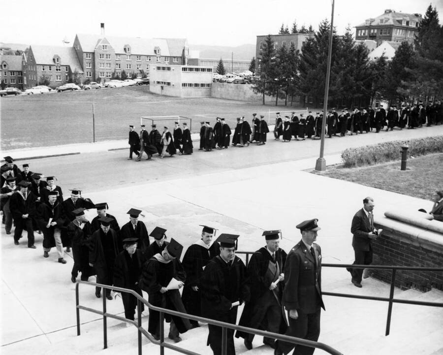 A photograph detailing two lines of students as they make their way toward the entrance of Memorial Gymnasium for University of Idaho's commencement.