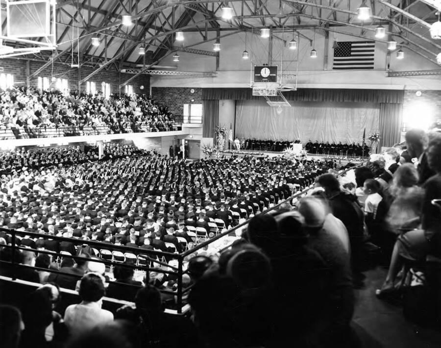 A photograph taken of University of Idaho's commencement ceremonies from within the audience in the back corner of the Memorial Gymnasium.