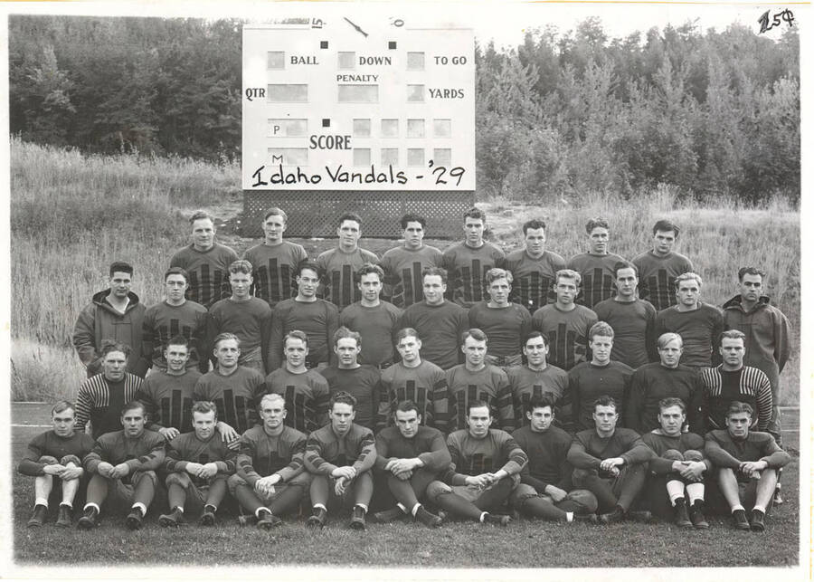 Photograph featuring the 1929 Idaho Vandals football team posing in front of its old scoreboard at MacLean Field.