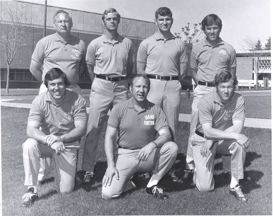 The Vandal coaching staff poses for a photograph on the grass in front of the campus library. Coaches pictured: Front) Don Matthews, Don Robbins, Tom Roth; Back) Ed Troxel, Gary Knecht, Hoyt Keeney, Tom Manke.