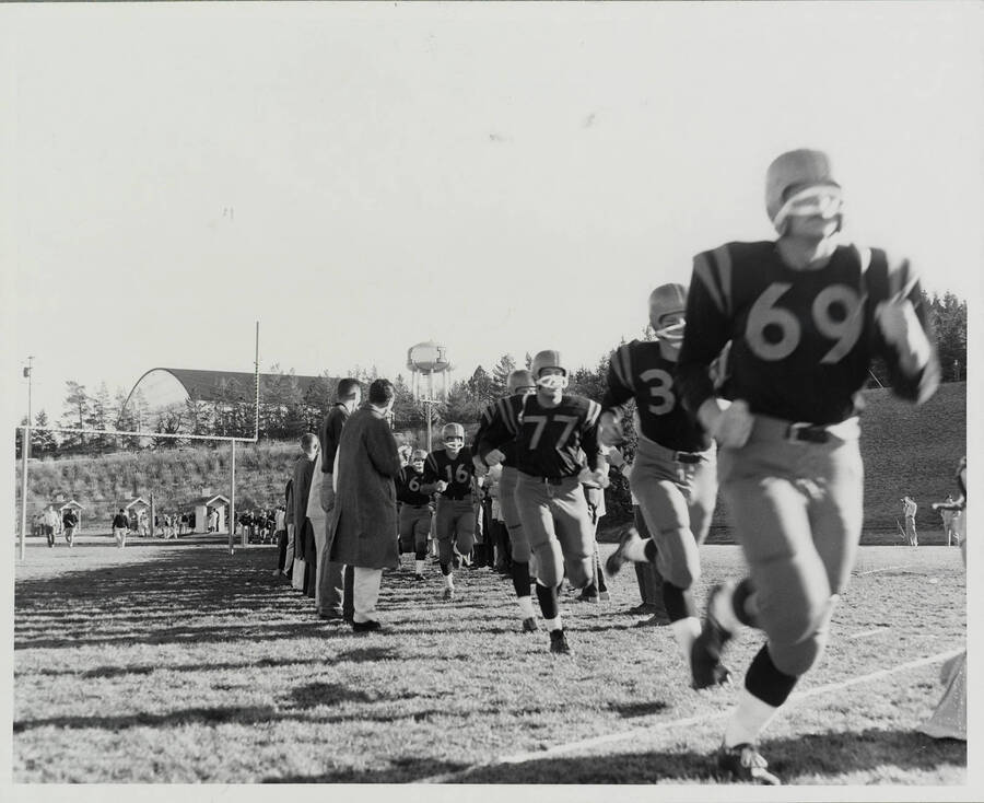 Players going onto field. Football game, University of Idaho vs. Washington State University.; Idaho football takes the field in a column formation. The water tower can be seen in the background.