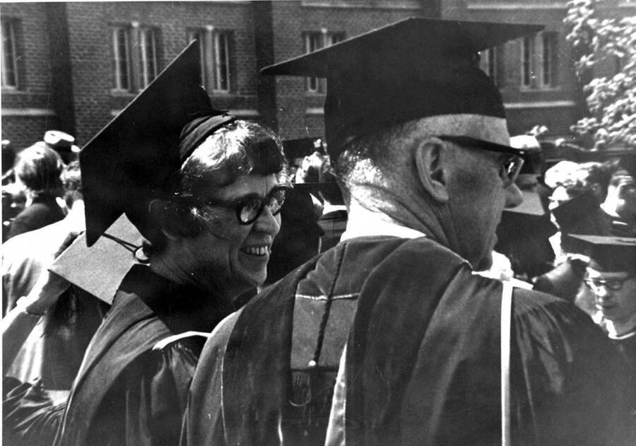 Two faculty members smile and talk while watching students gather for the traditional procession into the Commencement ceremony.
