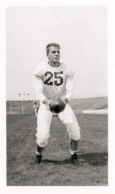 George Eidam (#25), a freshman football player for the University of Idaho, holding the ball on the field as a teammate runs behind him.