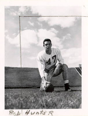 Center for the University of Idaho football team, Bob Hunter (#47) kneeling with his hand on a football on the field.