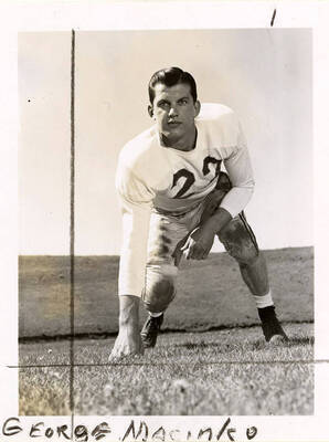George Macinko (#22), end for the University of Idaho football team, crouching with a hand on the football field.