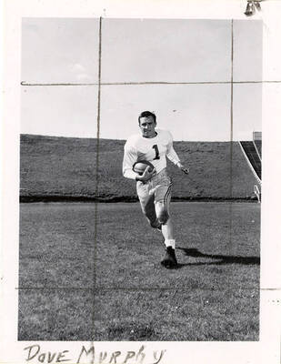 Dave Murphy (#1), right halfback for the University of Idaho football team, running with a football on the field.