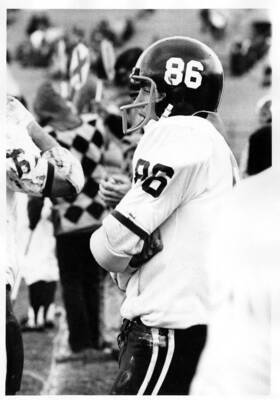 A football player for the University of Idaho stands on the sidelines with his arms crossed during a football game.