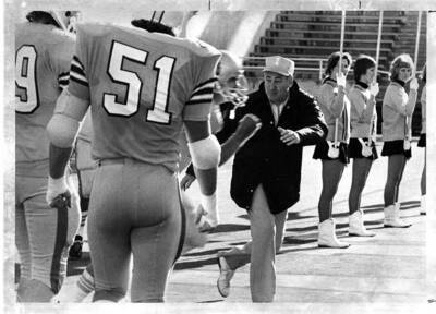 A coach runs next to his players as girls holding flags look on.