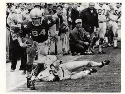 A football player runs with the ball as his opponent lays behind him after a failed tackle attempt.