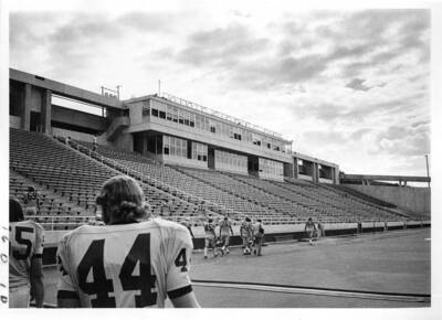 University of Idaho football players in full uniform walk onto the football field surrounded by empty bleachers.