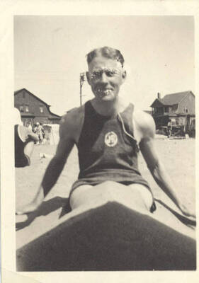 A man sits on the beach with the camera balanced in front of him on his legs.