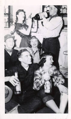 Unidentified fraternity members dressed in Western clothing sit together during a party.