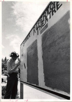 A man paints 'Summer Repertory Theatre' on a wooden board.