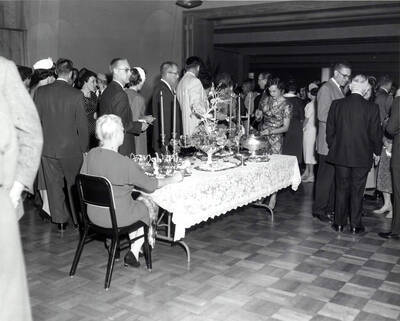 A woman sits at a table set with a floral centerpiece and a silver tea set during the faculty reception.