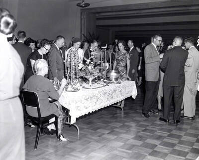 A woman sits at a table set with a floral centerpiece and a silver tea set during the faculty reception.