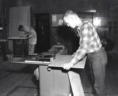 Two Industrial Arts Education students work at different machines in a wood shop.