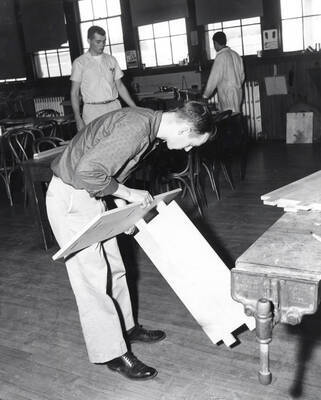 An Industrial Arts Education student pieces two pieces of wood together while two other students work in the background.