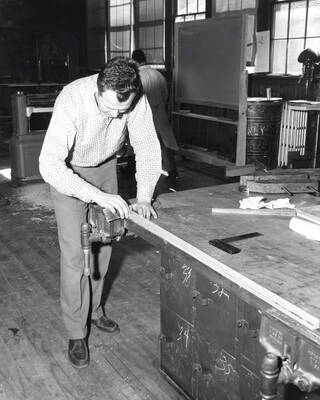 An Industrial Arts Education student sands a piece of wood laid out on a table.