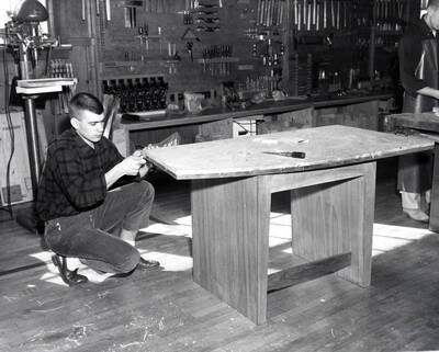 An Industrial Arts Education student works with a plank of wood as part of his table project while another student works beside him.
