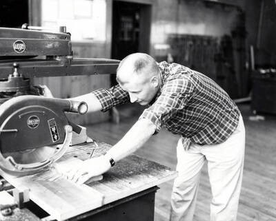 An Industrial Arts Education student uses a radial arm saw to cut a piece of wood in the shop.