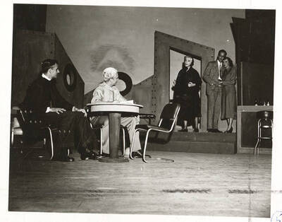 Performers identified from left -r: Guy Terwilleger as Rev. William Duke, Hugh Burgess as Rev. Frank Thompson, Larraine Cole as Mrs. Misget, Robert Bunting as Henry and Mary Thompson as Ann. Ann and Henry grasp each other while  listening to a speech Mrs. Misget gives to the reverends in Idaho drama's production of 'Outward Bound.' Presented by the University Players, an ASUI production directed by Jean Collette.