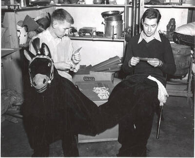 Two Idaho drama performers sit and play cards prior to the production of 'Sing, Senator, Sing.' An ASUI production written by Geoffrey Coope, Theodore Sherman, & music Hall Macklin (all UI teaching faculty), directed by Jean Collette in the University Auditorium.